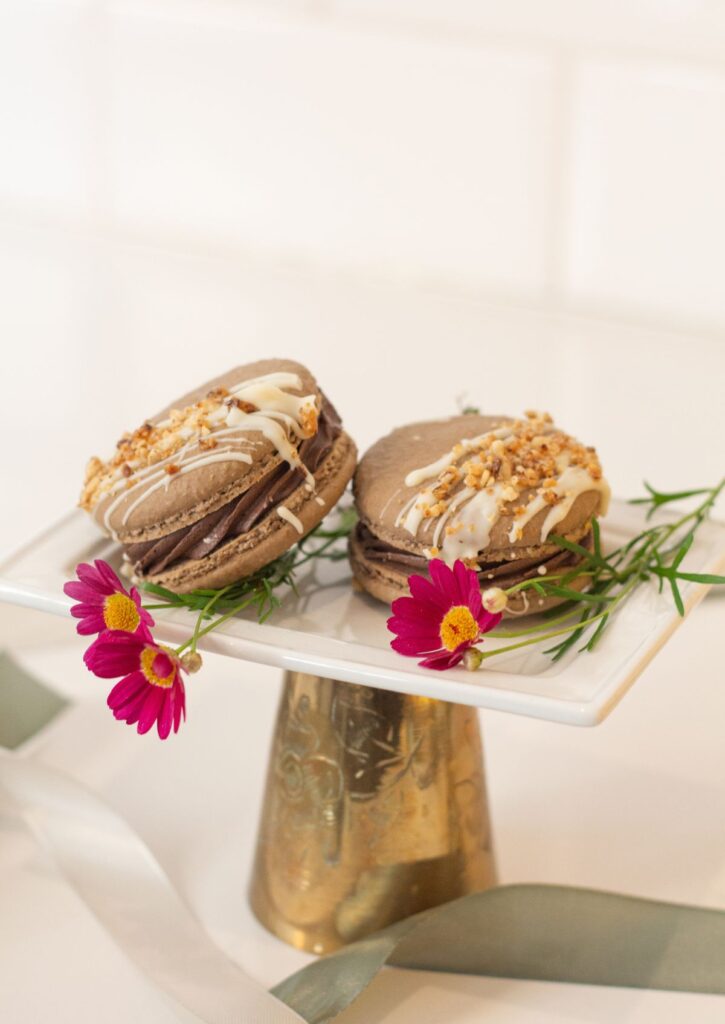 Giant Hazelnut Chocolate Macaron - two chocolate macarons with white chocolate drizzle and caramelized hazelnut topping on white gold cake stand
