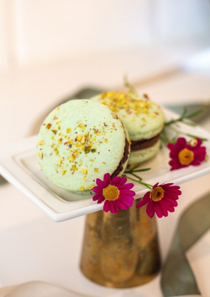 Giant Pistachio Cream Macaron - two mint green macarons with pistachio crumble and pink daisies on white gold cake stand