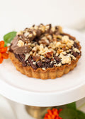 Pecan Chocolate Tart - side view on white cake stand with orange flowers